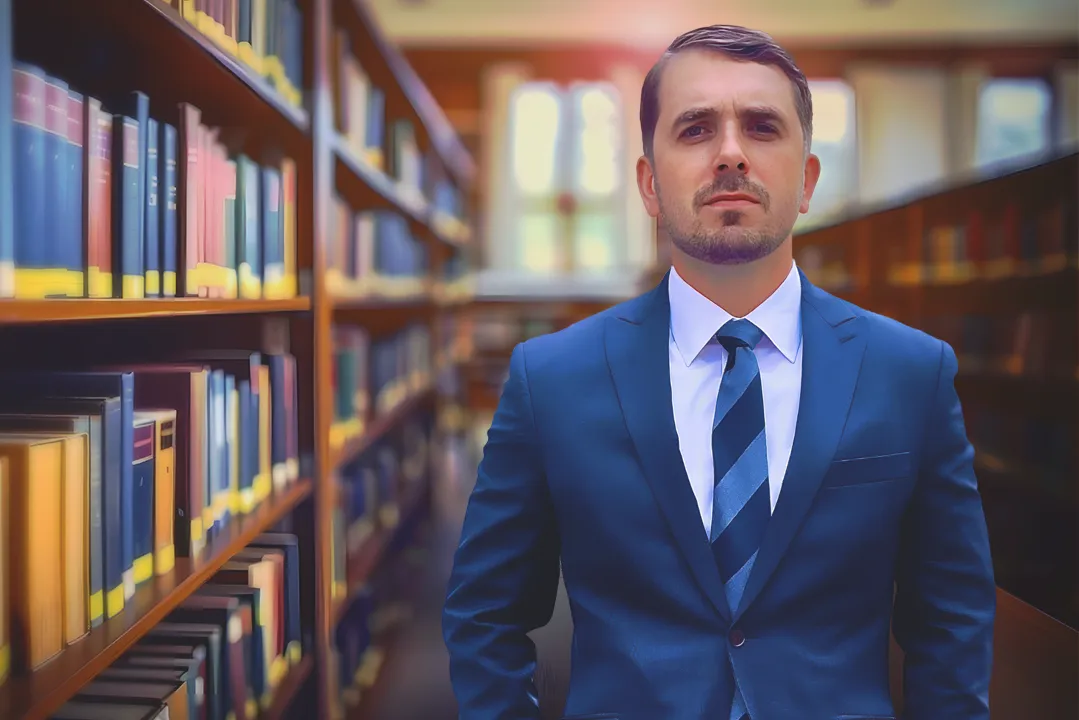 Attorney Piotr Burdzy in a blue suit standing in a law library, representing the personal injury team at Burdzy & Associates in New York.